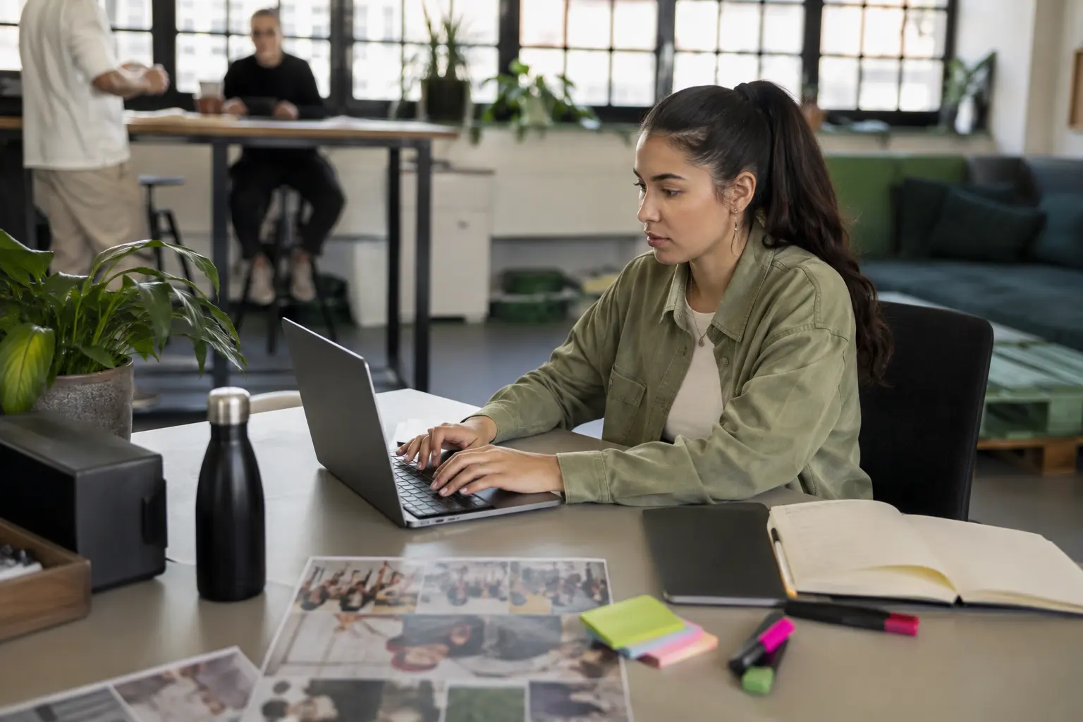 Studentin arbeitet am Laptop im offenen Büro, Notizbuch und Fotos auf dem Tisch