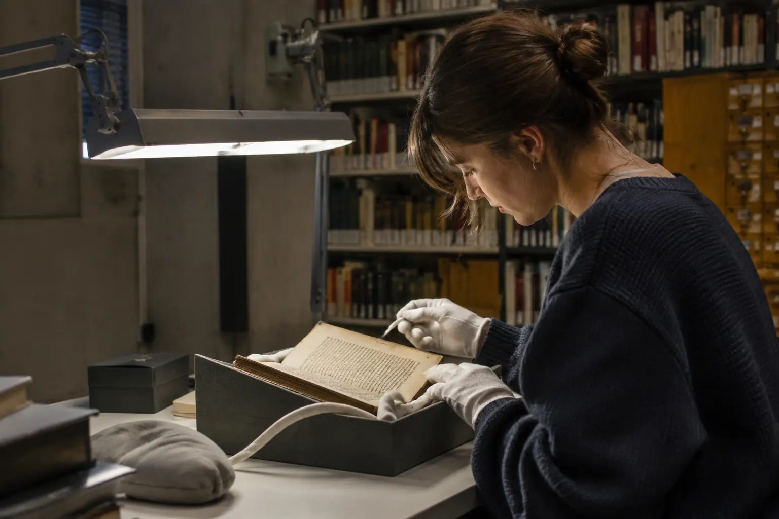 Studentin blättert mit Handschuhen in einem historischen Band im Archiv