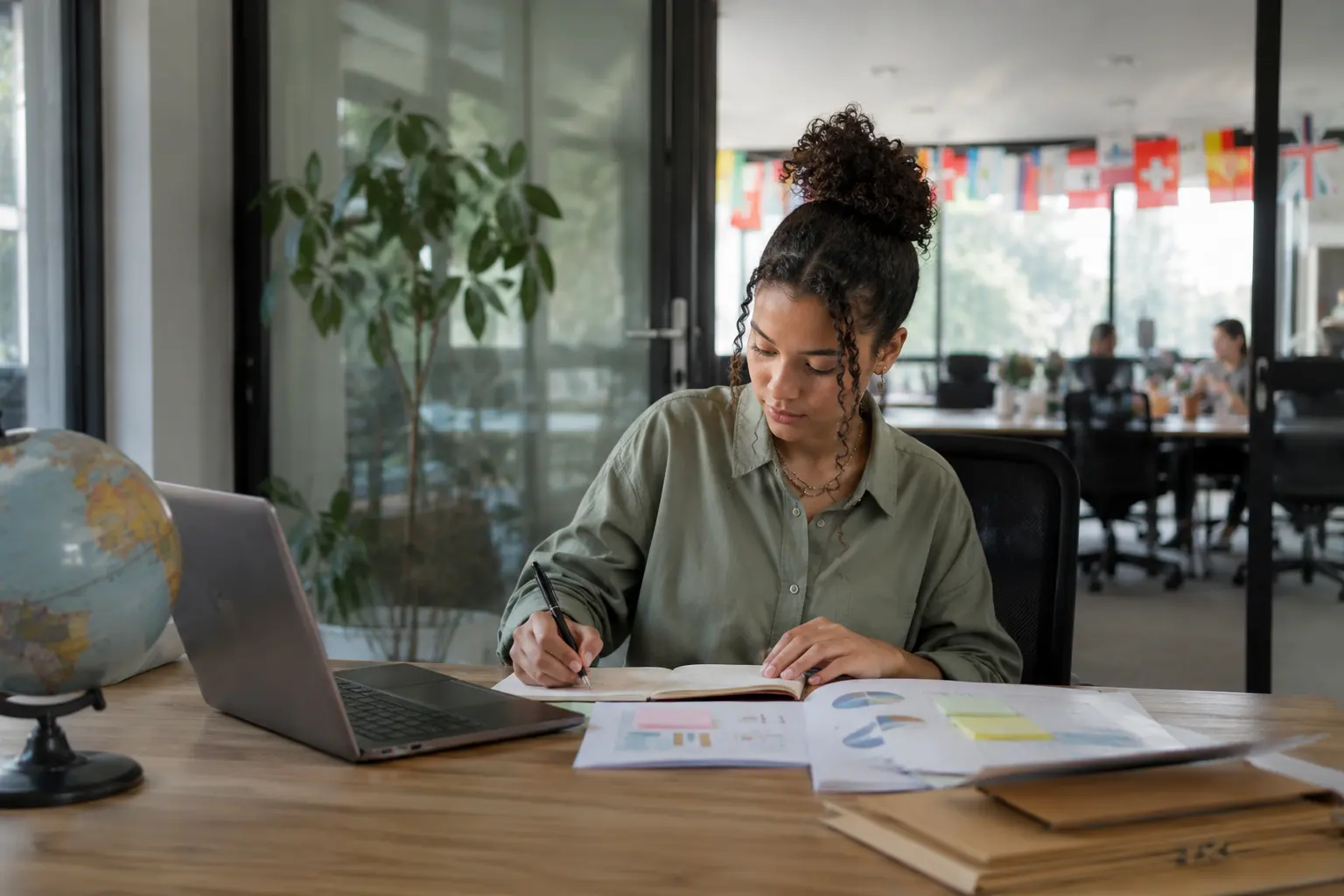 Studentin arbeitet am Laptop, Globus und Auswertungen auf dem Tisch