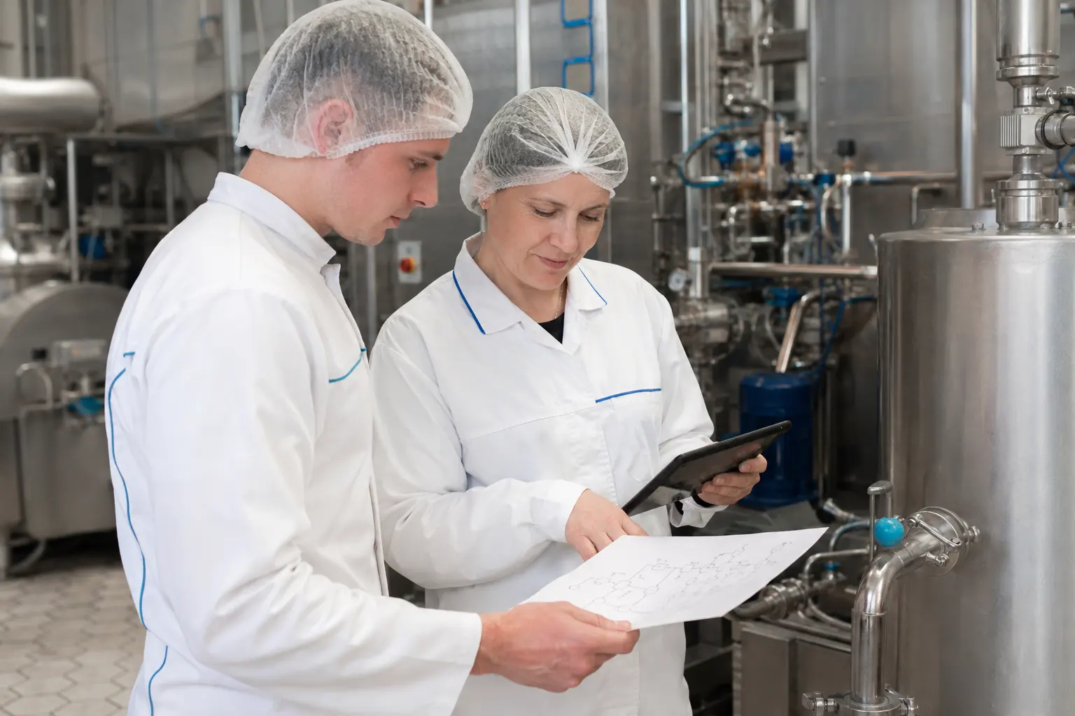 Zwei Milchtechnologen prüfen Unterlagen an der Produktionsanlage