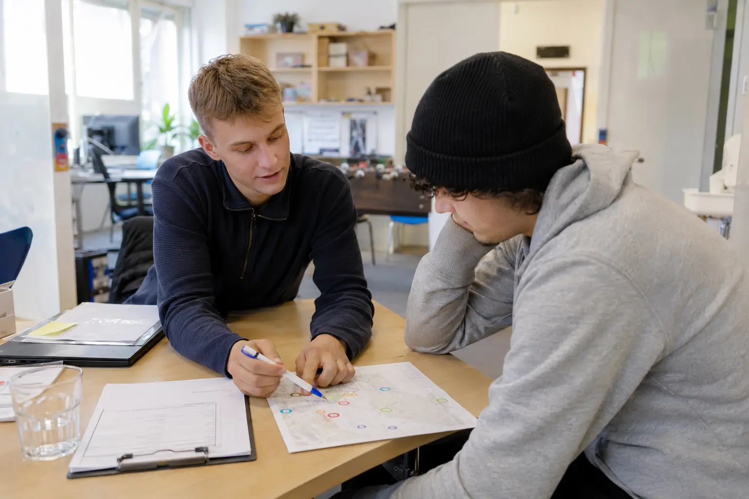Sozialarbeiter bespricht mit einem Jugendlichen einen Plan am Tisch